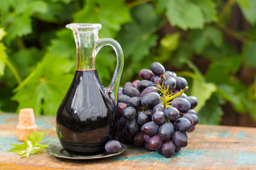 Black old balsamic vinegar in a glass jug with fresh red grapes on green vineyard background