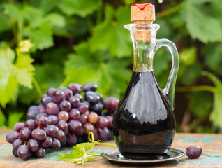 Black old balsamic vinegar in a glass jug with fresh red grapes on green vineyard background