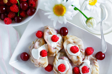 Sweet dumplings with cherries and raspberries. Dumplings with berries in white dish with sour cream. Top view