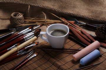 Cup of coffee, chalks and paint brushes on jute, linen sack 