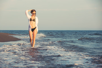 Attractive young woman walking along sea or ocean beach at sunset
