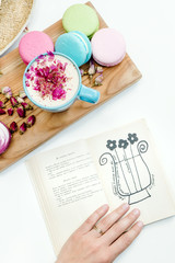Beauty girl hand with book. Morning aroma cappuccino drink and french macarons on wood desk