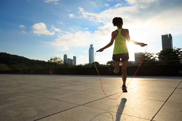 young fitness woman jumping rope on sunrise city building roof - obrazy, fototapety, plakaty