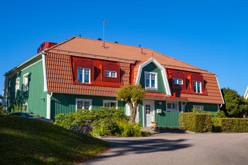 Residential house with massive roofs, green hedge in front on blue sky background.