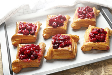 Tray with delicious puff pastries and cherry on wooden table