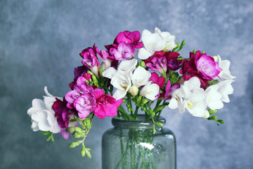 Vase with beautiful freesia flowers on color background