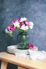 Vase with beautiful freesia flowers and kitchenware on light table