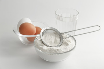 Bowl with flour, eggs and glass of water on white background