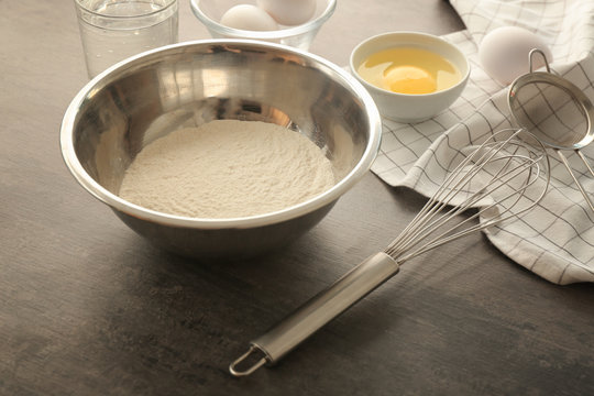 Metal bowl with flour and ingredients for dough on grey table