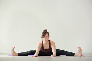 Fototapeta premium Young woman practicing yoga on light background indoors
