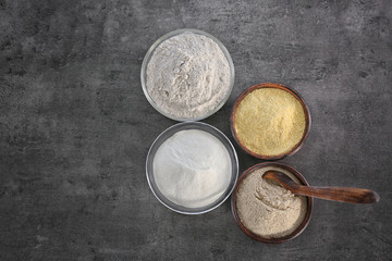 Bowls with different types of flour on gray background