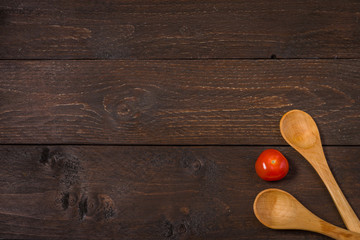 Two wooden spoons on a dark wood background and vegetables red cherry tomatoe vitamins delicious in the middle. Vegeterian or vegan background.