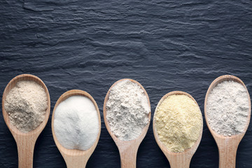 Wooden spoons with different types of flour on dark background