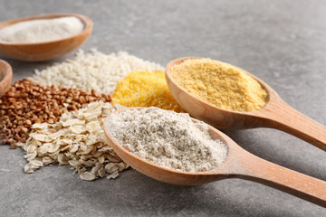 Wooden spoons with different types of flour on gray background