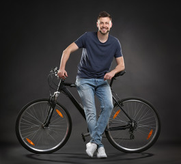 Fototapeta na wymiar Handsome young man with bicycle on dark background