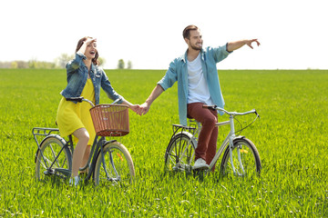 Happy young couple riding bicycles in green field