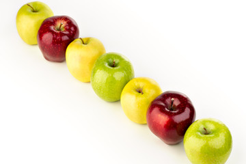 Multicolored apples in a row on a white table