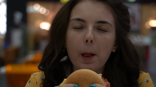 The Girl Is Eating A Burger On A Food Court.