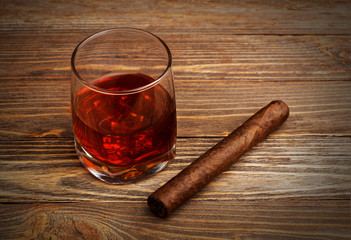 Glass of whiskey with ice cubes and cigar on a wooden table. Vignette