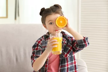 Crédence de cuisine en verre imprimé Jus Cute little girl drinking juice while sitting on sofa at home