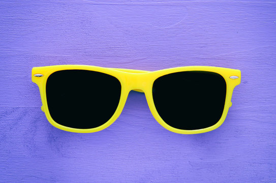 Hipster yellow sunglasses on purple wooden background