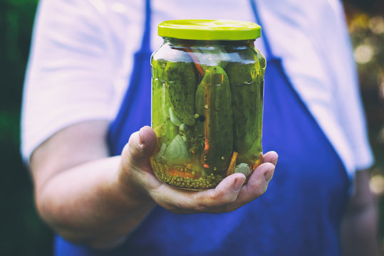 Senior woman holding a jar of pickles in the garden. Homemade pickled cucumbers in a glass jar. Preserving jar of gherkins with mustard seeds and dill. 