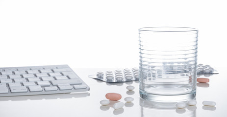 Gesundheit, Medizin, Tabletten, Wasserglas und Tastatur spiegelnd auf heller Tischplatte