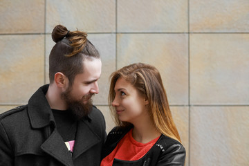Handsome young male hipster with hairbun standing close to his beautiful girlfriend and looking at her with love, feeling happy. Couple having fun, spending date outdoors, walking and chatting