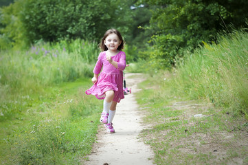 Adorable little girl in pink dress runs in the forest. Sunny day