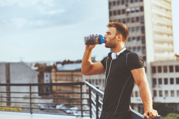 Young man resting on the roof of the building after workout and drink water - Powered by Adobe