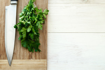 Fresh organic parsley with knife on wooden cutting board.
