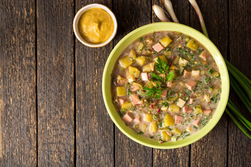 Okroshka. Traditional Russian summer cold soup with sausage, vegetables and kvass in bowl on wooden background.