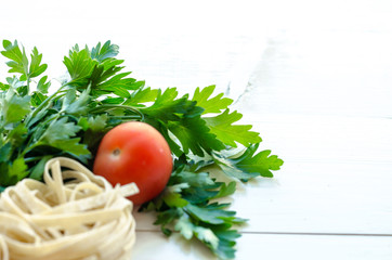Tagliatelle with ingredients for cooking pasta. Curly parsley, garlic, tomatoes on a wooden table.