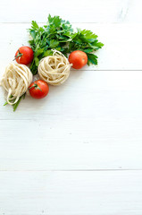 Fototapeta na wymiar Tagliatelle with ingredients for cooking pasta. Curly parsley, garlic, tomatoes on a wooden table.