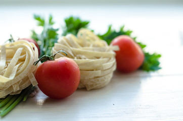 Tagliatelle with ingredients for cooking pasta. Curly parsley, garlic, tomatoes on a wooden table.