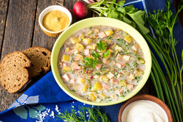 Okroshka. Traditional Russian summer cold soup with sausage, vegetables and kvass in bowl on wooden background.
