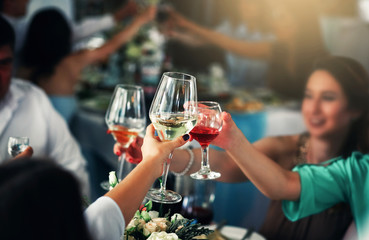 Closeup photo of hands clinking glasses with wine at party.