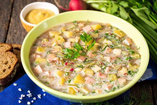 Okroshka. Traditional Russian summer cold soup with sausage, vegetables and kvass in bowl on wooden background.