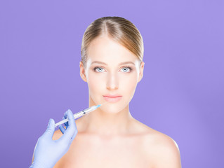 Young and beautiful woman having skin injections over magenta background. Plastic surgery concept.