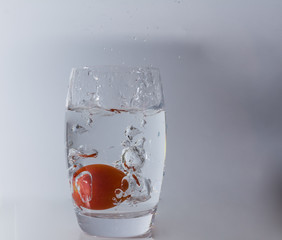 Tomate fällt in das Glas mit Wasser