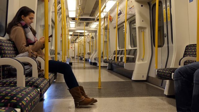 Girl travelling by tube, metro or underground train sitting in almost empty carriage and using her smartphone   