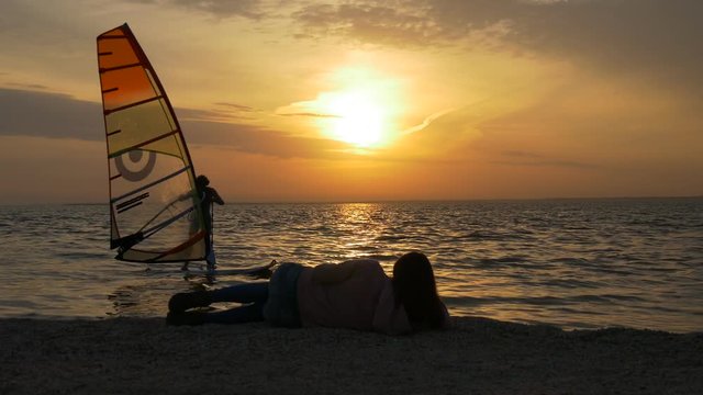 Woman looks at windsufer on sunset from beach