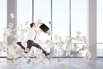 Businessman jumping in an office lobby, papers