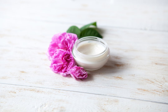 Pot of beauty cream surrounded by flowers on white wooden table