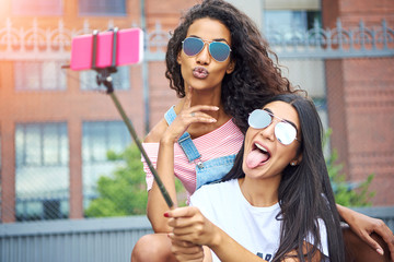 Carefree girlfriends making face and taking selfies outside