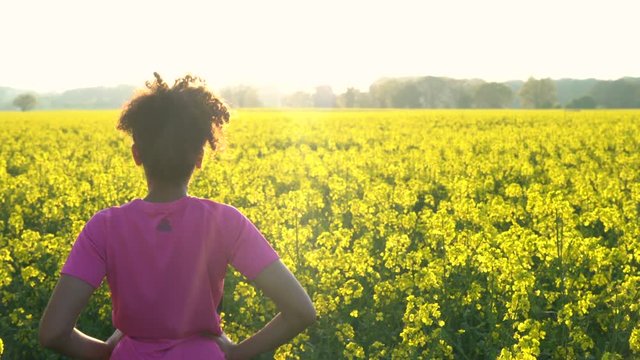 Jib or crane 4K video clip of beautiful healthy mixed race African American girl teenager female young woman running or jogging and standing in field of yellow flowers