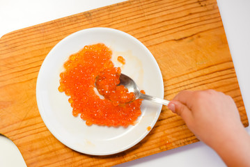 Closeup on person eating red caviar delicacy from white plate, closeup light macro background