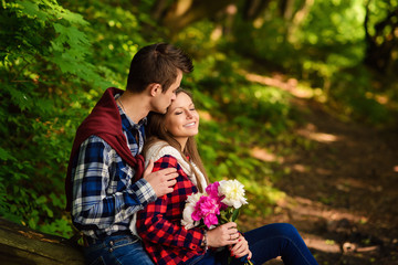 Stylish young couple in shirts and jeans while walking in the forest. A handsome boyfriend kisses his beautiful charming girlfriend on the forehead.