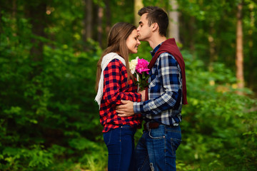 Fototapeta premium Stylish young couple in shirts and jeans while walking in the forest. A handsome boyfriend kisses his beautiful charming girlfriend on the forehead.