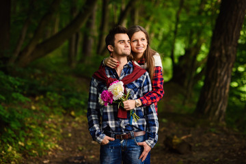 Fototapeta premium Stylish young couple in shirts and jeans while walking in the forest. Beautiful charming girl hugs her handsome boyfriend.